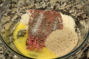 In a mixing bowl, combine the ground beef, egg, salt, ground black pepper, pesto, grated asiago cheese, grated Parmesan cheese, and breadcrumbs.