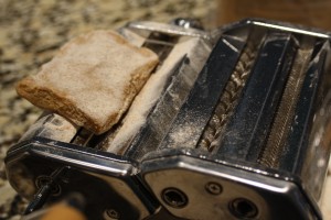 Next on the widest setting of your pasta machine (usually the largest number, my largest is a number 7), insert the dough and use the crank to roll through.  I use my left hand to crank and my right hand to catch the pasta coming out.