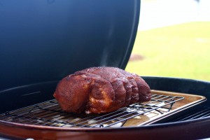 Preparing your smoker/charcoal grill, follow your manufacturer’s instructions for indirect heating.  You’ll want a temperature of 275-300 degrees Fahrenheit.  Here, we’ve placed a pan with water and chopped onions, with a baking rack under the pork.